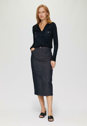 Donkerdenim midi-rok met een rechte snit, zijzakken en een knoopsluiting. Gecombineerd met een aansluitend zwart shirt met lange mouwen en zwarte slides.