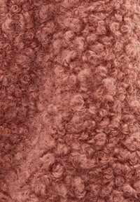 Tessuto testurizzato in una morbida tonalità rosa-bruna. La superficie presenta un motivo riccio e soffice, che aggiunge profondità e interesse tattile.