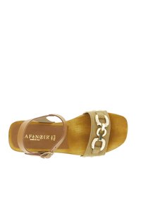 Beige sandaal met een platte zool, leren strip en decoratieve gouden kettingdetail. Heeft een gesloten teen en een verstelbare enkelband.