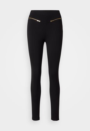 Leggings noirs avec une texture lisse, présentant deux poches zippées dorées à l'avant. Le design est ajusté et resserré aux chevilles.