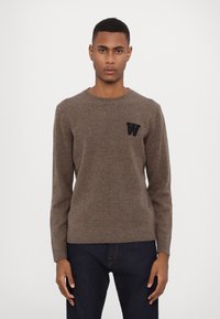 Brown knitted sweater with a crew neck, ribbed cuffs, and hem. Features a black embroidered "W" logo on the chest. Smooth texture.