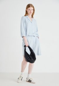 Camicia azzurro chiaro con bottoni e maniche tre quarti, abbinata a una gonna. Borsa nera e liscia e scarpe bianche con strisce nere.