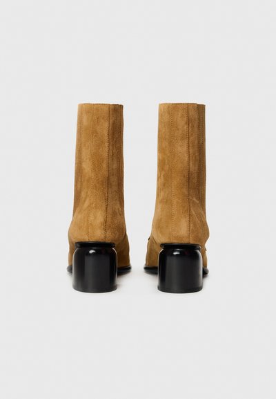 Bottes de cheville en suède marron avec une texture lisse, dotées d'un talon noir épais et d'un design de tige ajusté. Pas d'embellissements visibles.