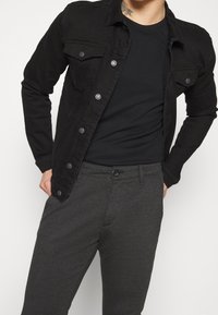Svart denimjacka med metallknappar, bröstfickor, kombinerad med mörkgrå byxor som har knappstängning och strukturerad tyg.