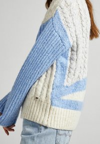 Neulepusero, jossa on sinivalkoinen väriblokkimalli. Hihansuissa resorikuvio ja vartalossa palmikkoneulepinta. Pehmeä ja miellyttävä materiaali.