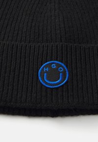 Zwarte geribbelde gebreide muts met een blauw geborduurd logo. De textuur is zacht, met een aansluitend ontwerp dat geschikt is voor warmte.