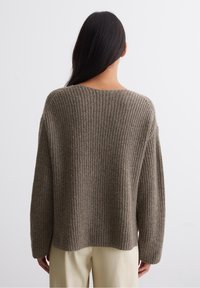 Bruine geribbelde gebreide trui met een ontspannen silhouet, brede halslijn en iets verlengde schouders. Zachte textuur en mouwlengte tot halverwege de arm.
