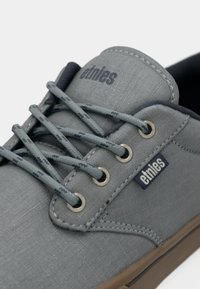 Γκρι καμβάς παπούτσι με μεταλλικές νημάτιες και επίπεδα κορδόνια. Διαθέτει λαστιχένια σόλα και ετικέτα λογότυπου στο πλάι. Λείο υλικό με ελάχιστο σχέδιο.