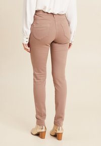 Tan, slim-fit broeken met een hoge taille, twee achterzakken en subtiele stiksels, gecombineerd met gouden, hoge hakken.
