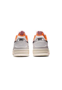 Baskets blanches et grises avec des accents orange ; caractéristiques : matériau texturé, col rembourré et logo noir. Silhouette basse et volumineuse.