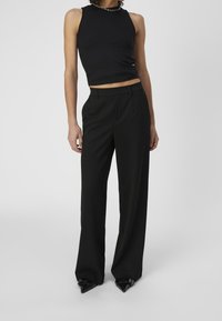 Czarny prążkowany crop top z wysokim kołnierzem zestawiony z dopasowanymi czarnymi spodniami, z prostą nogawką i wyraźnymi kantami, dopełniony spiczastymi butami.