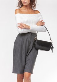 Top bianco a spalla scoperta con costine abbinato a pantaloni corti grigi a righe verticali a vita alta. Accessoriato con una piccola borsa nera.