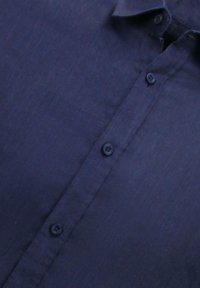 Navyblauwe linnen shirt met een knoopsluiting aan de voorkant, zes knopen en een subtiele textuur. De kraag ligt plat tegen de stof.