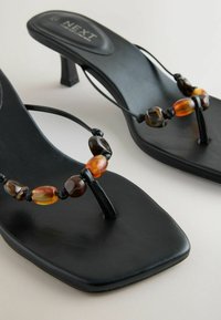 Sandales à talons noires avec bouts carrés et perles décoratives de couleur ambre sur des fines brides.