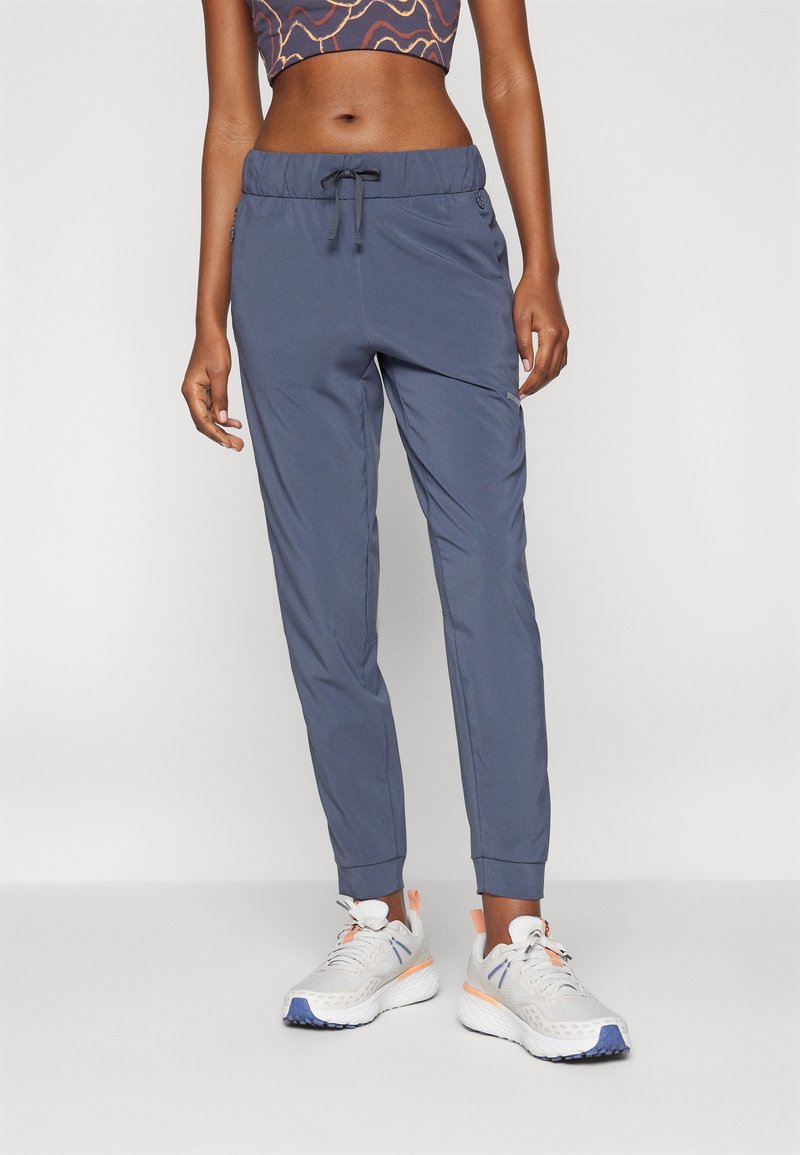 Gray athletic pants with an elastic waistband, drawstring, tapered legs, and side pockets, paired with light sneakers.