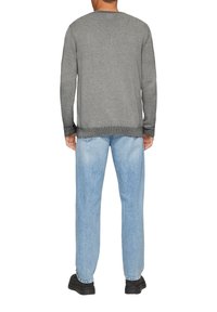 Grauer Strickpullover mit rundem Kragen, gerippten Bündchen und Saum, kombiniert mit hellblauen Jeans und schwarzem Schuhwerk.
