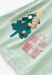 Pärlbroderad julgran med pom-pom dekorationer och en pärlbroderad rosa presentlåda på ljusgrön tyg med små vita trämönster.