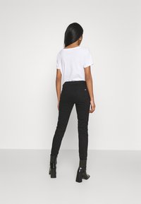 Jean noir taille haute en denim, silhouette ajustée, associé à un t-shirt blanc uni. Chaussures : bottines noires à talons épais.