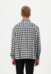 Black and white checkered flannel shirt with long sleeves, button cuffs, and a relaxed cut, featuring a yoke seam across the back.