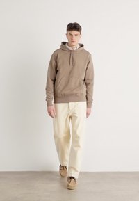 Bruine hoodie met een kangoeroezak en trekkoord, gecombineerd met crèmekleurige relaxte broek en lichtbruine schoenen.