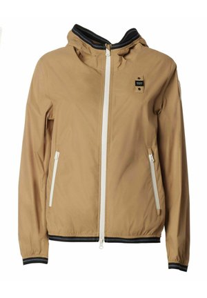 Giacca a vento beige con cappuccio, cerniera bianca, due tasche laterali e polsini a strisce nere. Leggera, con una texture liscia e un design casual.