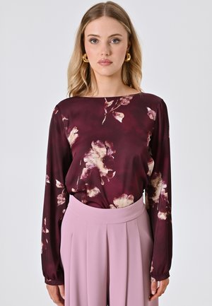 Langärmlige bordeauxfarbene Bluse mit Blumenmuster und Rundhalsausschnitt, kombiniert mit hoch taillierten, plissierten Hosen in zartem Rosaton.