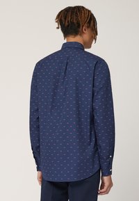 Navyblauw shirt met een klein roze hondenpatroon, lange mouwen, knoopmanchetten en een rugpasontwerp voor een betere pasvorm en structuur.