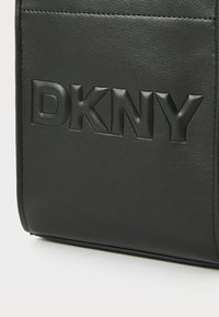 Črna usnjena torba z embosiranim logotipom "DKNY". Gladka tekstura z čistimi linijami in kontrastnim šivom, strukturirana oblika, minimalističen dizajn.