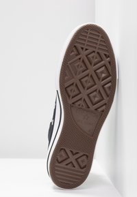 Czarne trampki na płaskiej podeszwie z brązowym gumowym podeszwa. Posiadają białe paski po bokach i oczka, a także teksturowany wzór podeszwy oraz logo "Converse All Star".
