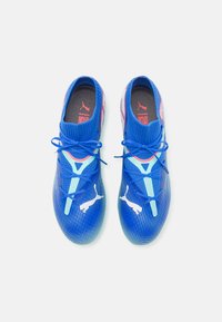 Blue athletic shoes with a textured mesh upper, featuring pink accents and white branding. Lace-up design with a cushioned insole.