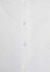 Camicia bianca con un motivo floreale ricamato, sei bottoni sulla parte anteriore e un tessuto morbido e strutturato.