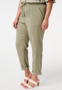 Pantalons légers vert clair, avec une taille élastique, un cordon de serrage et des poches latérales. Avec des poignets aux chevilles, ils présentent une texture lisse.