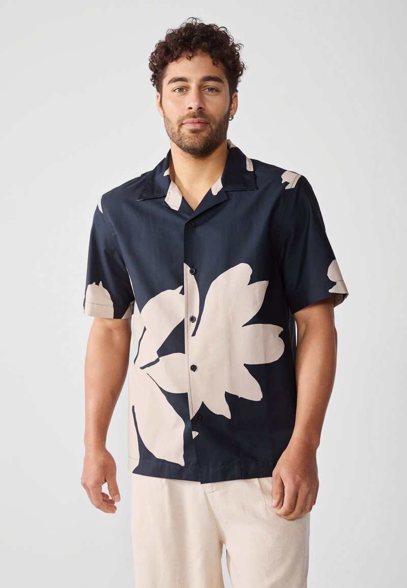 Camisa de manga corta, con botones, en azul marino con grandes patrones florales en beige, hecha de una tela suave, con cuello.