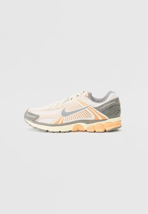 Chaussure de course blanche, grise et orange avec une tige en mesh et synthétique, semelle amortie et logo Nike Swoosh sur le côté.