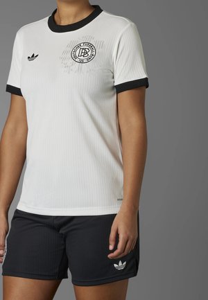 Valkoinen urheilupaita mustilla resorikraalla ja -hihoilla, jossa on logo rinnassa. Yhdistetty mustiin shortseihin, joissa myös logo.