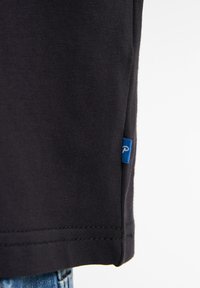 Zwart katoenen t-shirt met een rechte zoom, geribbelde textuur en een klein blauw label aan de zijkant. Close-up van de stof en de stiksel details.