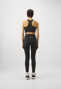 Svart sport-bh med racerback-design, kombinerad med högmidjade svarta leggings. Båda plaggen har en slät textur och minimal branding.
