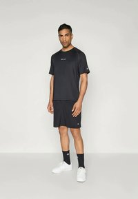 Černé sportovní tričko s krátkým rukávem a logem, spárované s odpovídajícími šortkami. Doplňky zahrnují černé ponožky a bílé tenisky. Jednoduchý, funkční design.