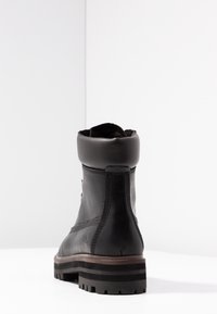 Botte en cuir noir avec un col arrondi, un design à lacets et une semelle en caoutchouc rainurée. La vue arrière montre les détails de la couture et un accent de logo.