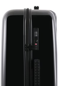 Black hardshell suitcase with a glossy finish, dual black zippers, a combination lock, and a raised textured grip along the side.
