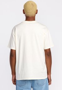Camiseta de manga corta color crema con un ajuste relajado, fabricada en algodón suave. Presenta un cuello redondo y un diseño minimalista sin gráficos ni patrones.