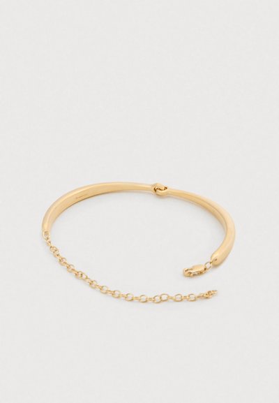 Bracelet jonc en ton or avec un design lisse et courbé, doté d'une rallonge chaîne et d'un fermoir sécurisé. La finition polie souligne l'élégance.