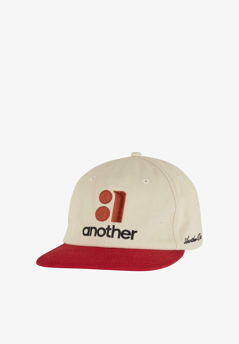 Beige bomullsmössa med en röd skärm. Har broderad "01" och "another" i svart och röd. Inkluderar ögla ventilationshål och en knapp på toppen.