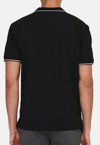 Schwarzes Polo-Shirt mit kontrastierendem weißen Besatz entlang des Kragens und der Ärmel, kurzen Ärmeln und einem lässigen Schnitt.