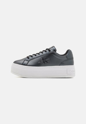 Sneakers platform in sintetico nero con texture liscia, caratterizzati da lacci neri, punta rotonda e suola bianca ondulata. Logo impresso di lato.