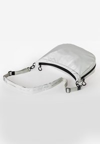 Weißer wasserdichter Beutel mit geschwungener Form, schwarzem Reißverschluss und verstellbarem Schulterriemen, ausgestattet mit Metallbeschlägen und einer glatten, matten Oberfläche.