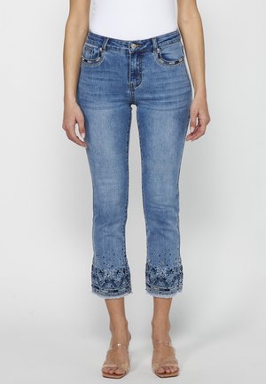 Lyseblå denim jeans med en tætsiddende pasform, der har broderede blomstermønstre og flossede kanter. Lommer med kæde-accenter.