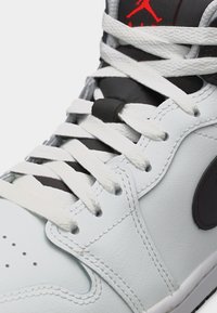 Άσπρο αθλητικό παπούτσι Air Jordan με μαύρη γλώσσα και κόκκινο λογότυπο Jumpman, με άσπρα κορδόνια και λεπτομερείς ραφές στο δερμάτινο επάνω μέρος.