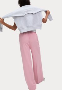 Grå bomullströja draperad över axlarna, tillsammans med rosa vida byxor med elastisk midja. Slät tygtextur.