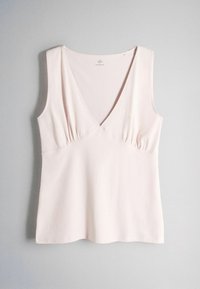 Débardeur rose pâle sans manches à col en V avec un tissu froncé sous la poitrine, suspendu sur un fond gris clair.